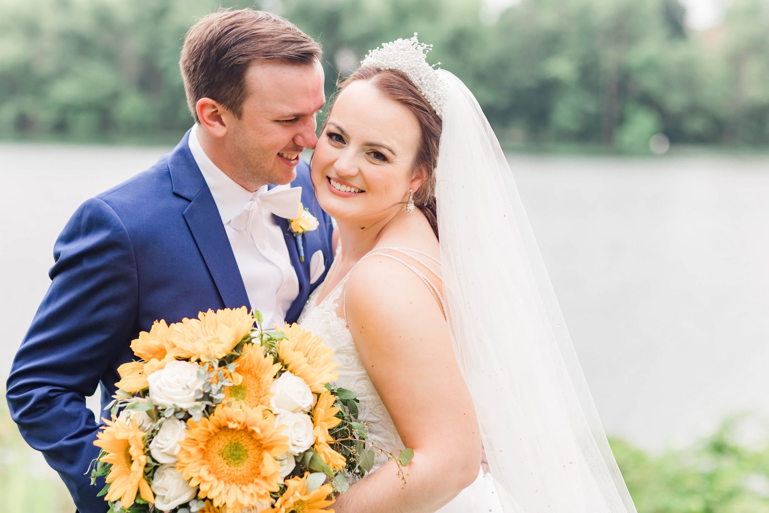 Bride and groom smiling at the camera with a sunflower bouquet.