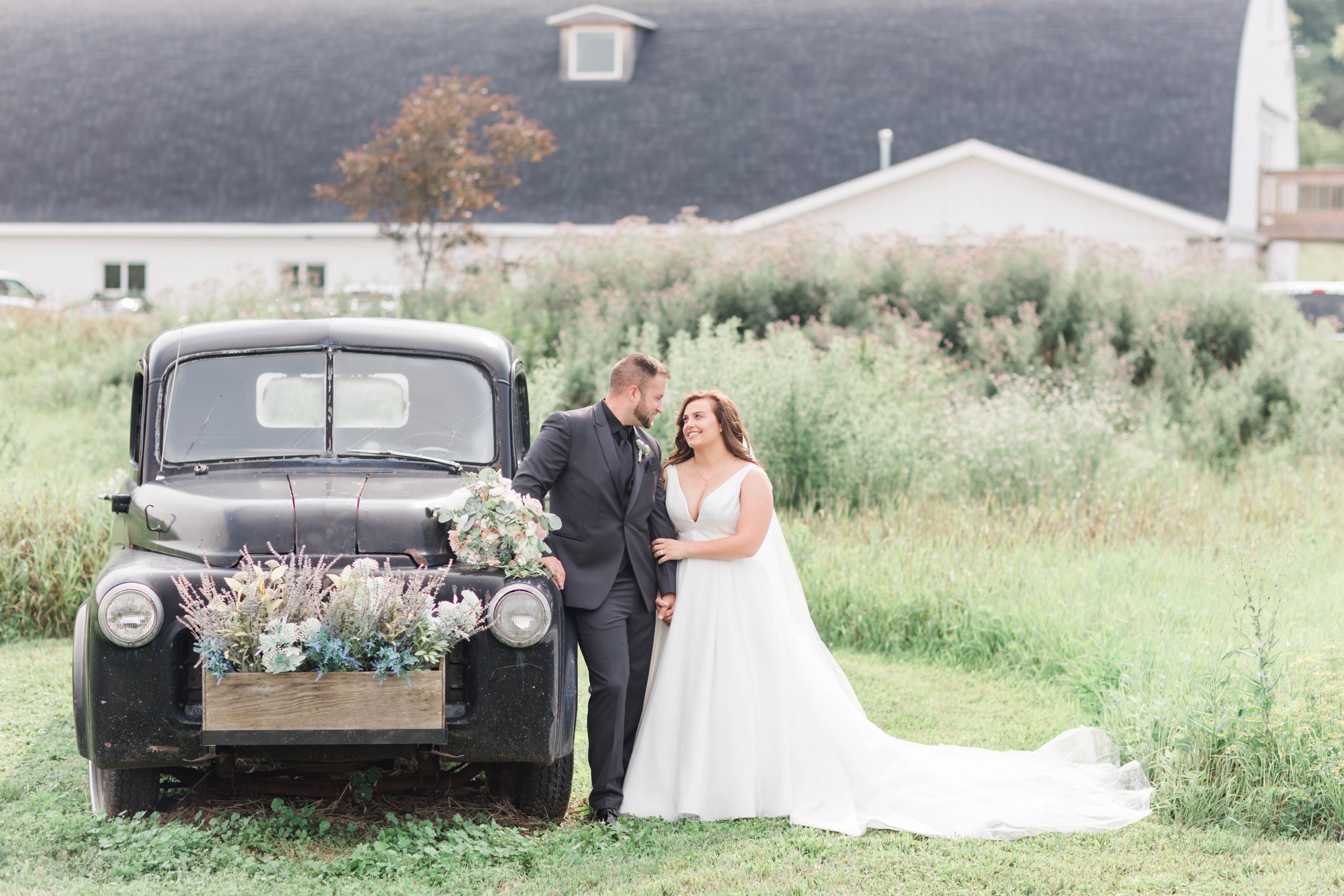 Bride and groom looking at each other smiling while standing next to a black vintage truck at the Bowery Barn wedding venue